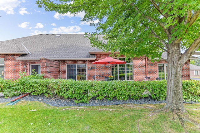 view of front of property with roof with shingles, brick siding, and a front lawn