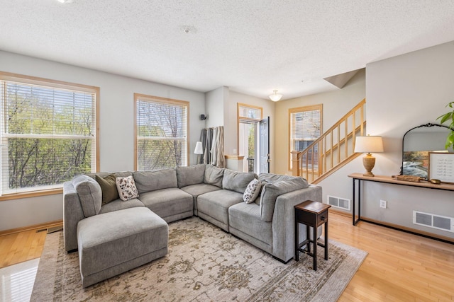 living room with stairway, visible vents, a textured ceiling, and wood finished floors