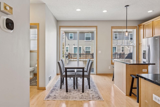 dining room with light wood finished floors, a textured ceiling, baseboards, and visible vents