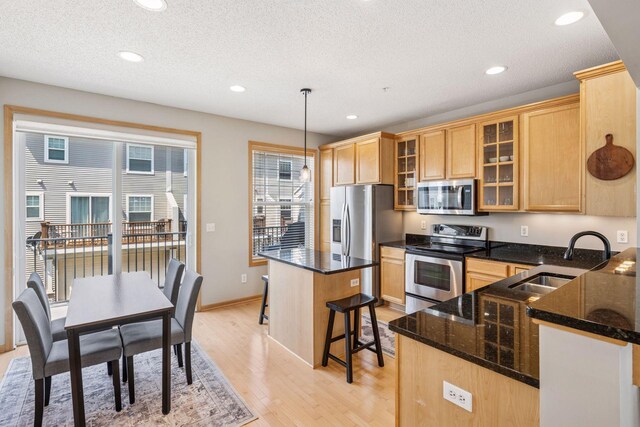 kitchen featuring a sink, dark stone counters, a kitchen breakfast bar, light wood finished floors, and appliances with stainless steel finishes