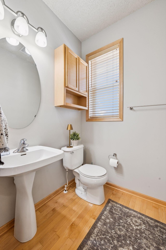 bathroom with toilet, a textured ceiling, baseboards, and hardwood / wood-style floors