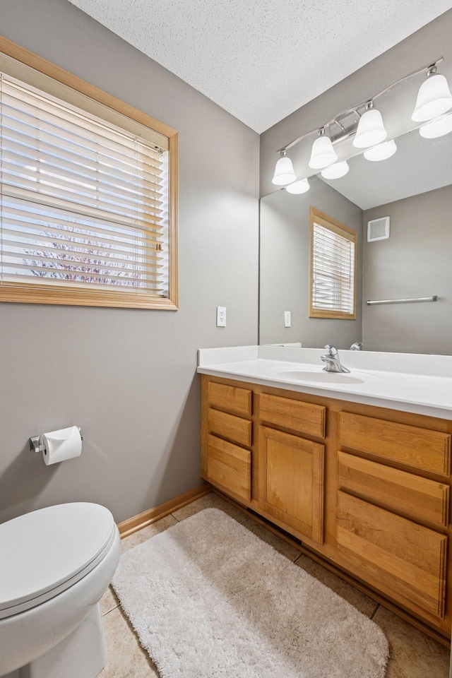 bathroom with toilet, vanity, visible vents, tile patterned floors, and baseboards