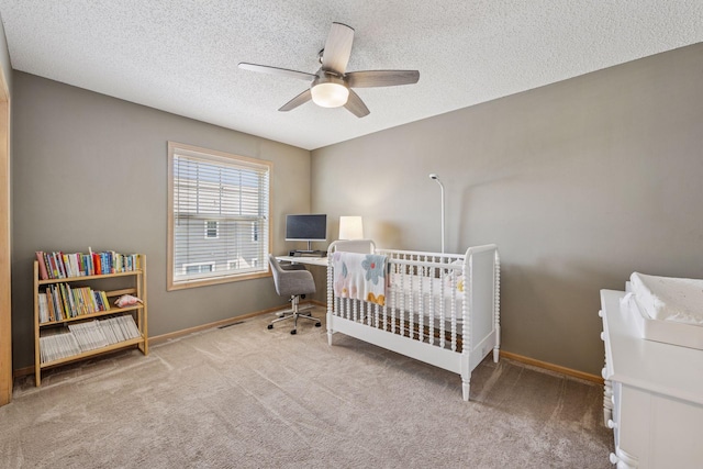 carpeted bedroom featuring baseboards, a nursery area, ceiling fan, and a textured ceiling