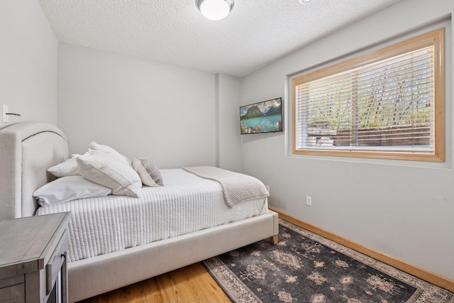 bedroom with a textured ceiling, baseboards, and wood finished floors