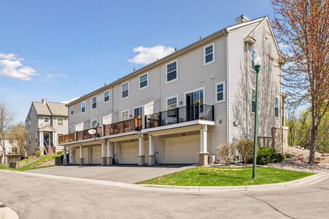 rear view of property featuring a balcony, driveway, and a garage