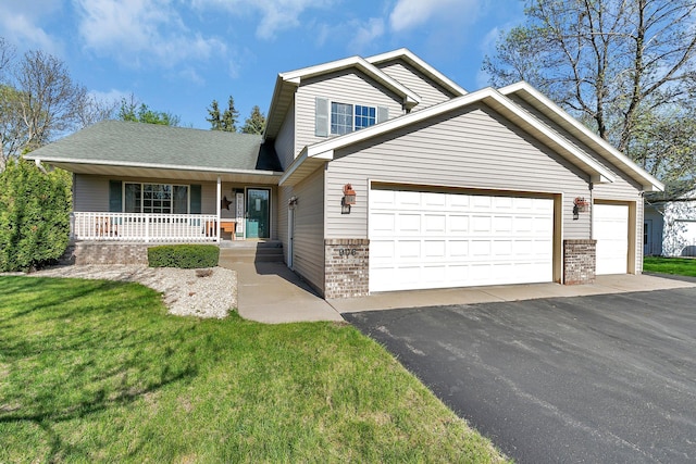 traditional home featuring brick siding, covered porch, an attached garage, driveway, and a front lawn
