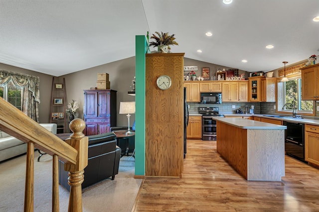 kitchen featuring black appliances, lofted ceiling, a sink, light countertops, and a center island