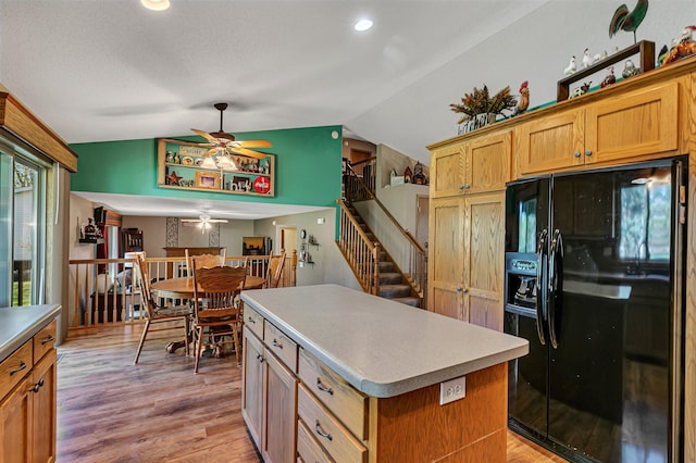 kitchen featuring black fridge with ice dispenser, a ceiling fan, a center island, vaulted ceiling, and light wood finished floors