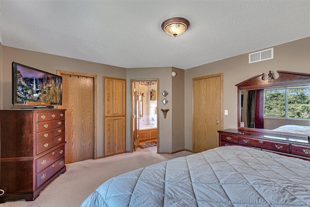 bedroom featuring light carpet, a textured ceiling, and ensuite bathroom