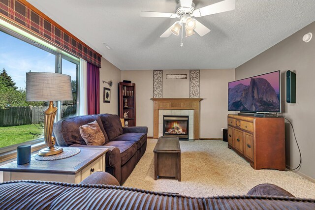 living room featuring light carpet, a fireplace, ceiling fan, baseboards, and a textured ceiling