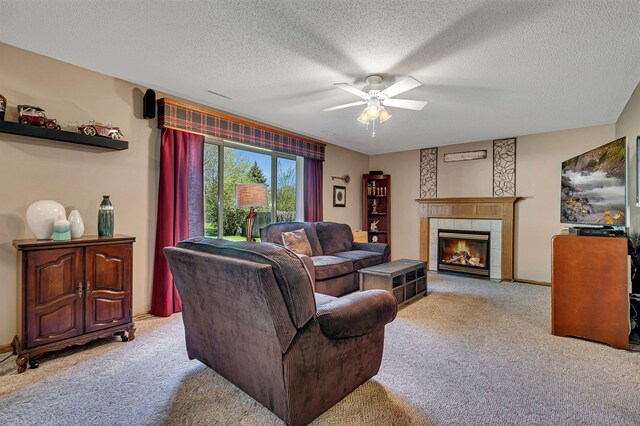 living area with light carpet, ceiling fan, a tiled fireplace, a textured ceiling, and baseboards