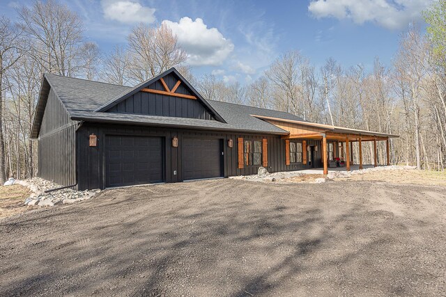 view of front of home with an attached garage, dirt driveway, roof with shingles, and board and batten siding