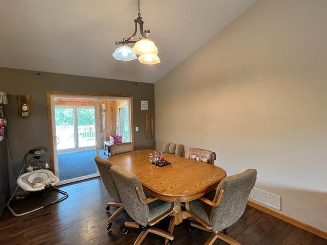 dining space with vaulted ceiling, baseboards, visible vents, and dark wood finished floors