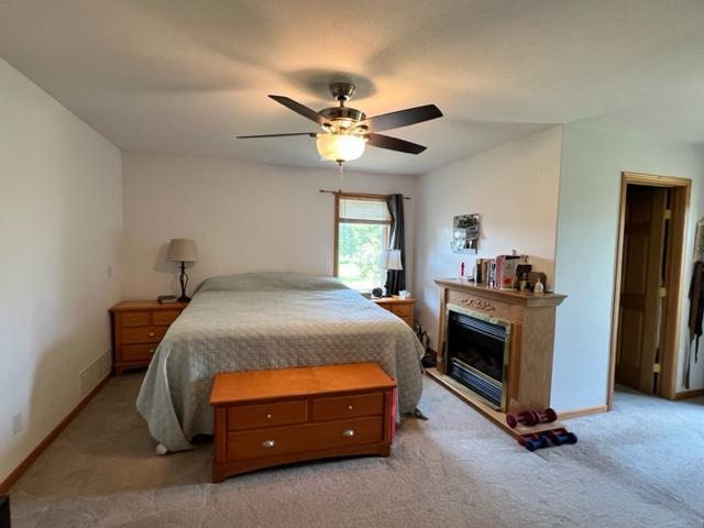 bedroom with light colored carpet, baseboards, a ceiling fan, and a glass covered fireplace