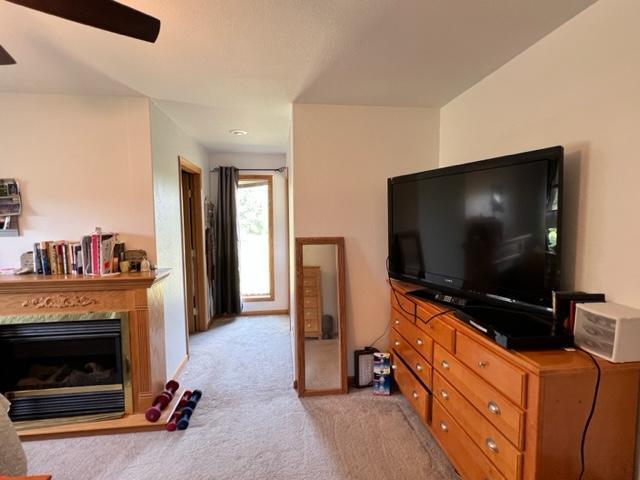 living area with a ceiling fan, light carpet, and a glass covered fireplace