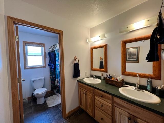 full bathroom with a sink, double vanity, toilet, and tile patterned floors