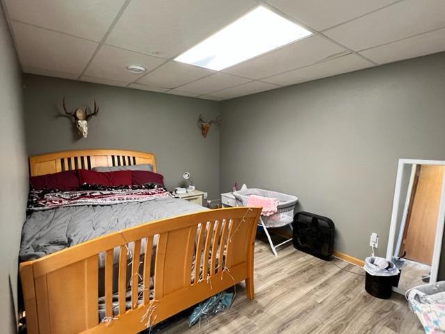 bedroom with a paneled ceiling, baseboards, and wood finished floors