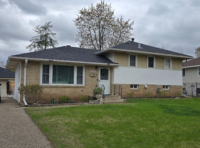 tri-level home featuring a shingled roof, brick siding, and a front lawn