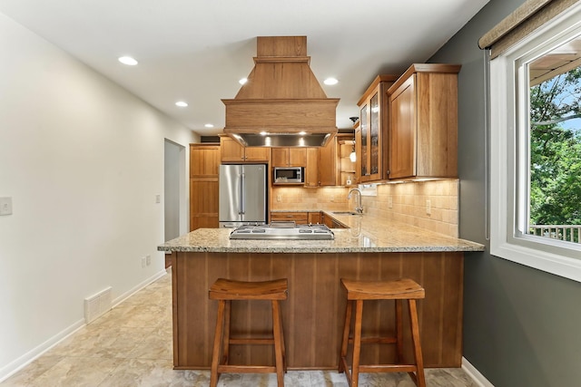 5820 139th St W, Apple Valley, MN 55124 - kitchen featuring stainless steel appliances, brown cabinetry, light stone counters, decorative backsplash, and glass insert cabinets