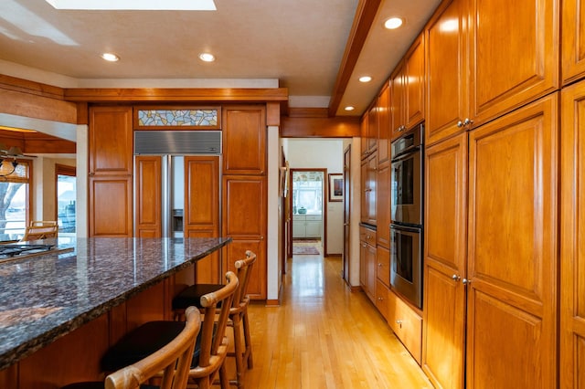 9002 Riley Lake Rd, Eden Prairie, MN 55347 - kitchen with double oven, brown cabinetry, a breakfast bar, light wood-type flooring, and recessed lighting