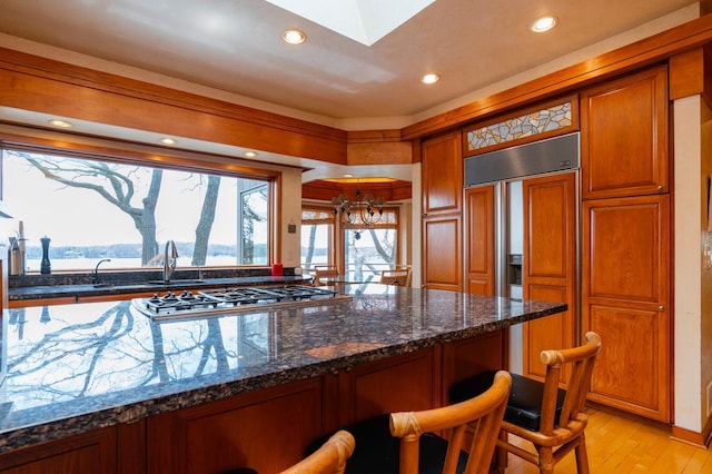 9002 Riley Lake Rd, Eden Prairie, MN 55347 - kitchen featuring brown cabinetry, paneled fridge, a kitchen breakfast bar, stainless steel gas stovetop, and light wood-type flooring