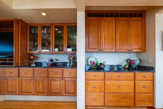 9002 Riley Lake Rd, Eden Prairie, MN 55347 - kitchen with brown cabinetry, dark stone countertops, glass insert cabinets, recessed lighting, and light wood-style flooring