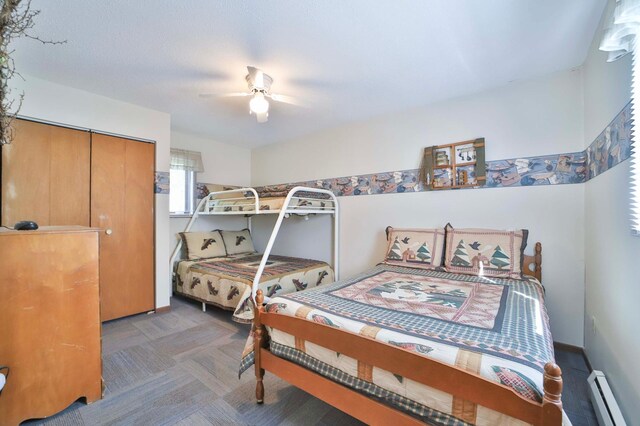 carpeted bedroom featuring a baseboard heating unit, a ceiling fan, and a closet