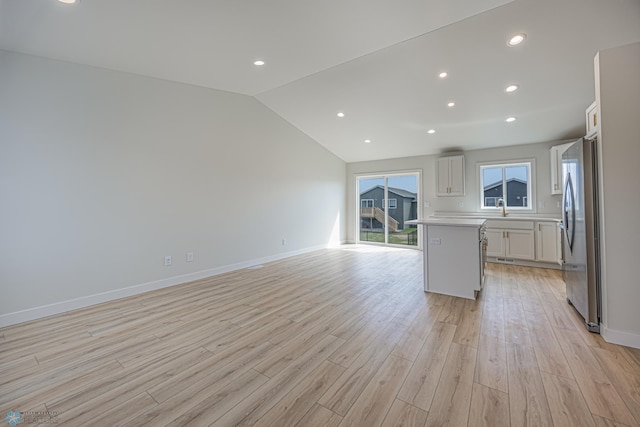 kitchen with freestanding refrigerator, light wood finished floors, light countertops, vaulted ceiling, and open floor plan