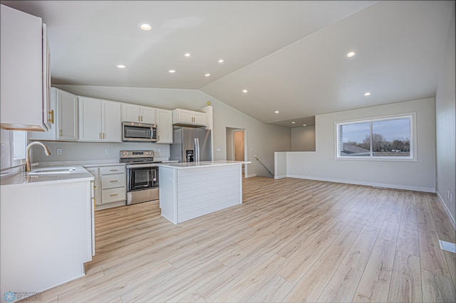 kitchen with appliances with stainless steel finishes, a sink, lofted ceiling, a kitchen island, and light countertops