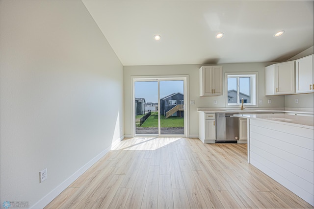 kitchen with stainless steel dishwasher, light countertops, light wood-style floors, white cabinets, and baseboards