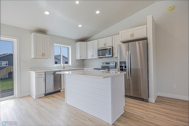 kitchen with appliances with stainless steel finishes, lofted ceiling, light countertops, light wood-style floors, and a center island