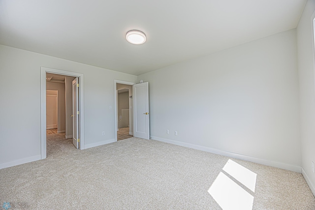 unfurnished bedroom with light colored carpet, baseboards, and a spacious closet