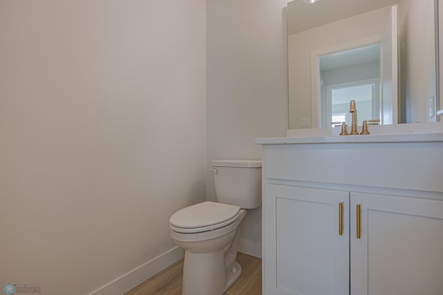half bathroom featuring baseboards, wood finished floors, vanity, and toilet