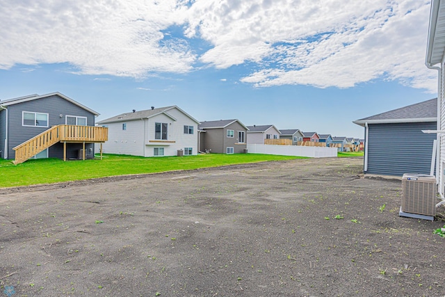 back of house featuring central AC unit, a wooden deck, a residential view, stairs, and a yard
