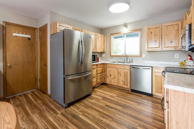 kitchen with stainless steel appliances, wood finished floors, a sink, and light brown cabinetry
