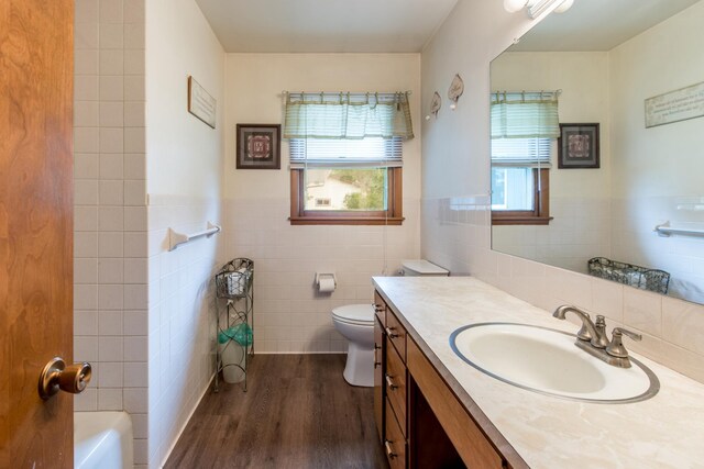 full bath with tile walls, toilet, wood finished floors, vanity, and a tub