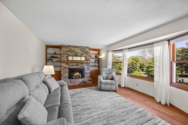 living room with a fireplace, light wood-type flooring, baseboards, built in features, and a textured ceiling