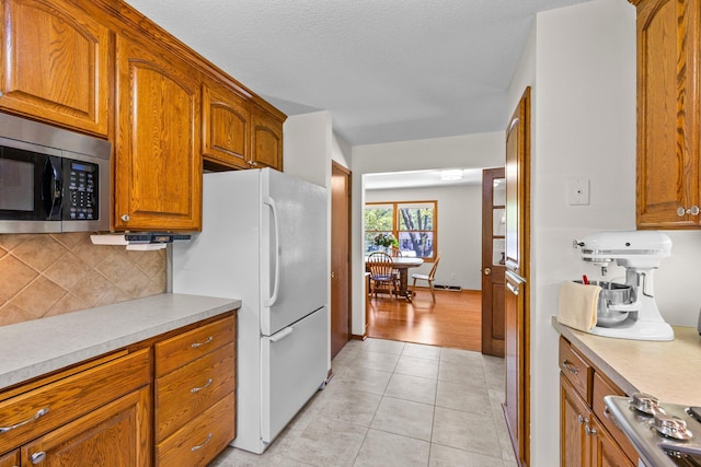 kitchen featuring stainless steel appliances, tasteful backsplash, brown cabinets, and light countertops