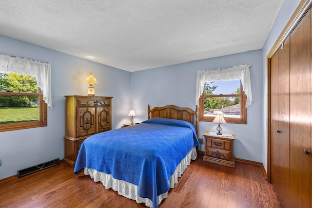 bedroom featuring a closet, a textured ceiling, wood finished floors, and baseboards