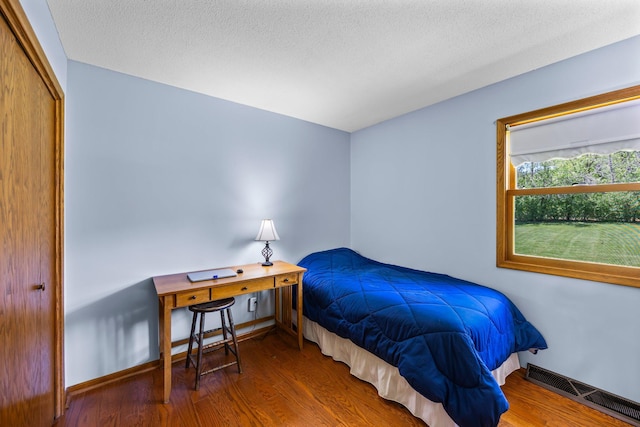 bedroom with wood finished floors, baseboards, and a textured ceiling