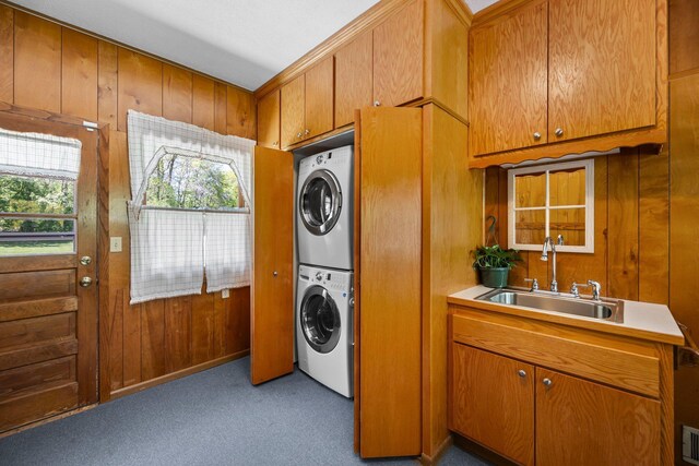 clothes washing area with stacked washer / drying machine, a sink, wooden walls, and carpet flooring