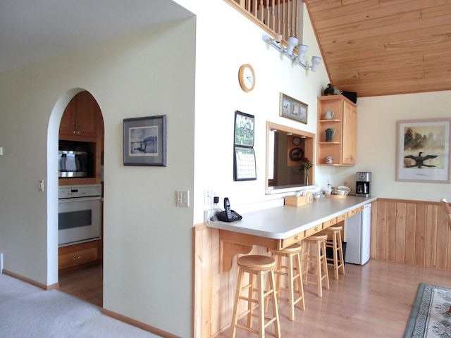 499 Tamarack Ct NE, Tenstrike, MN 56683 - kitchen with white oven, stainless steel microwave, light brown cabinetry, a breakfast bar area, and lofted ceiling