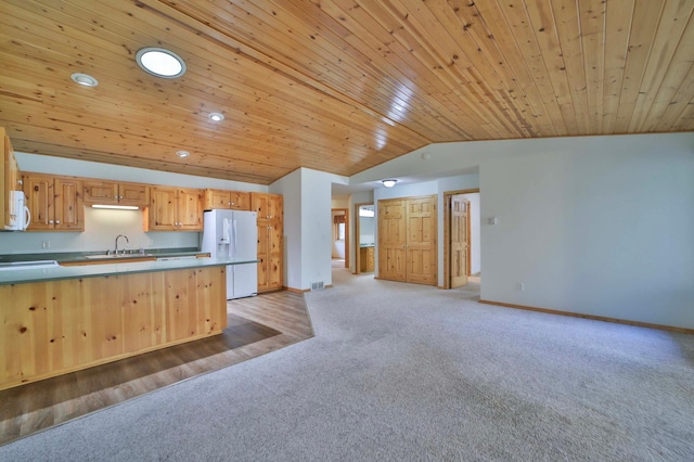 kitchen featuring white appliances, a sink, vaulted ceiling, light colored carpet, and baseboards