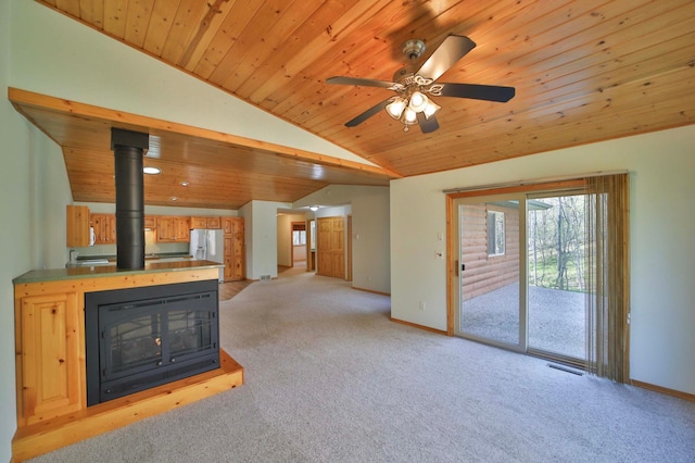 unfurnished living room featuring lofted ceiling, light colored carpet, wooden ceiling, baseboards, and a wood stove