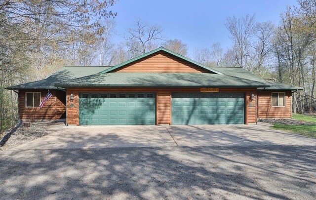 view of front of home with a garage, concrete driveway, a shingled roof, and faux log siding