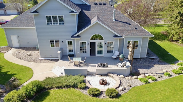 back of house featuring a lawn, a deck, a fire pit, and a shingled roof