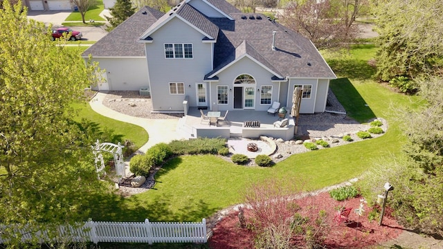 rear view of property featuring a yard, fence, an outdoor fire pit, a patio area, and roof with shingles