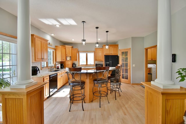 kitchen featuring a sink, decorative columns, black appliances, light wood finished floors, and a kitchen bar