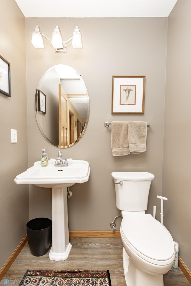 half bathroom with baseboards, wood finished floors, toilet, and a sink