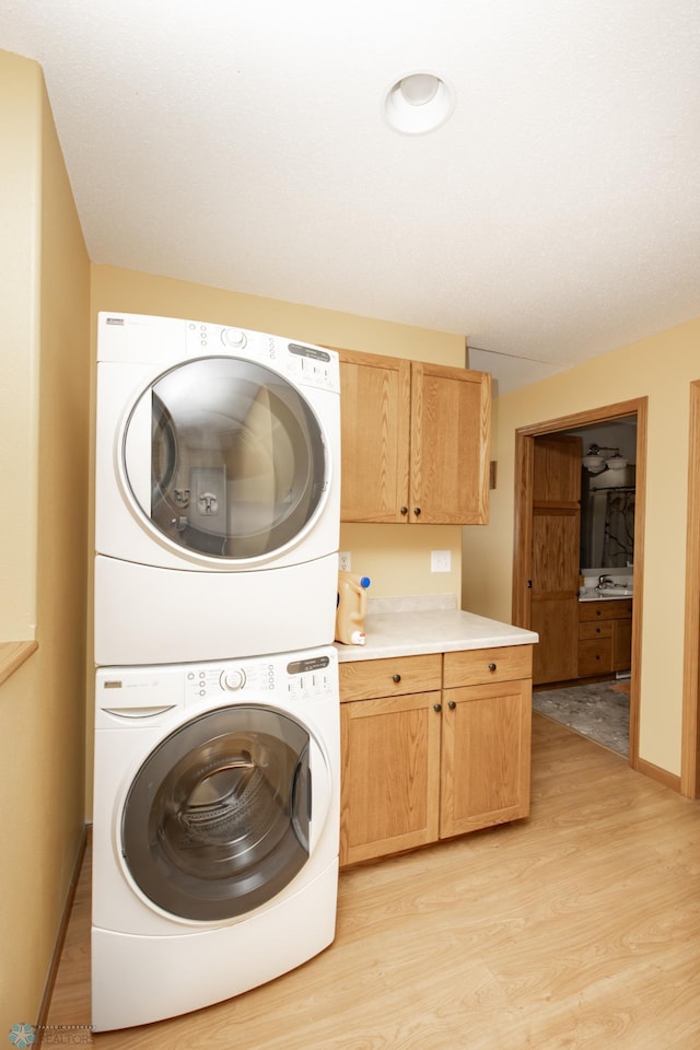 clothes washing area with stacked washing machine and dryer, cabinet space, and light wood finished floors